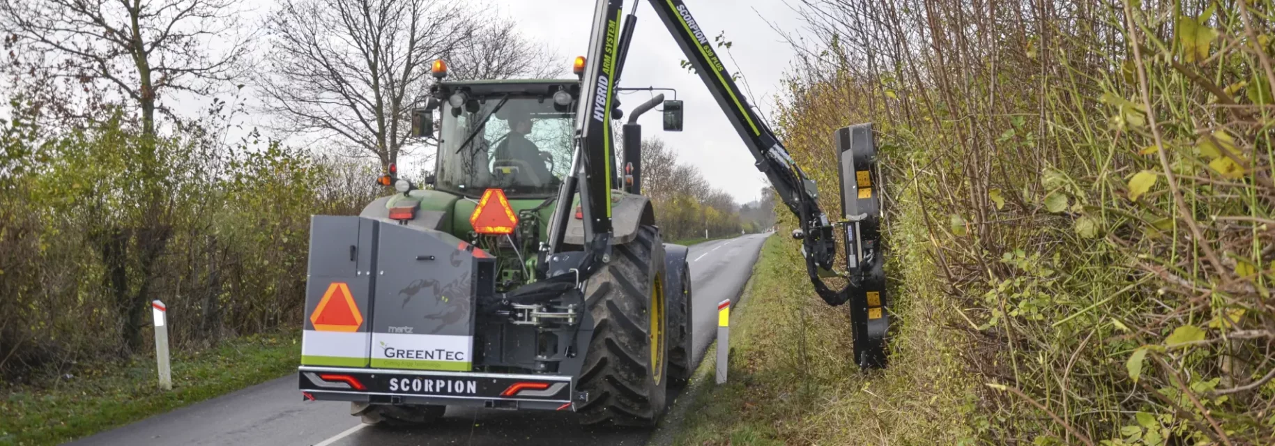 Vertical brush cutter attached to boom arm on tractor